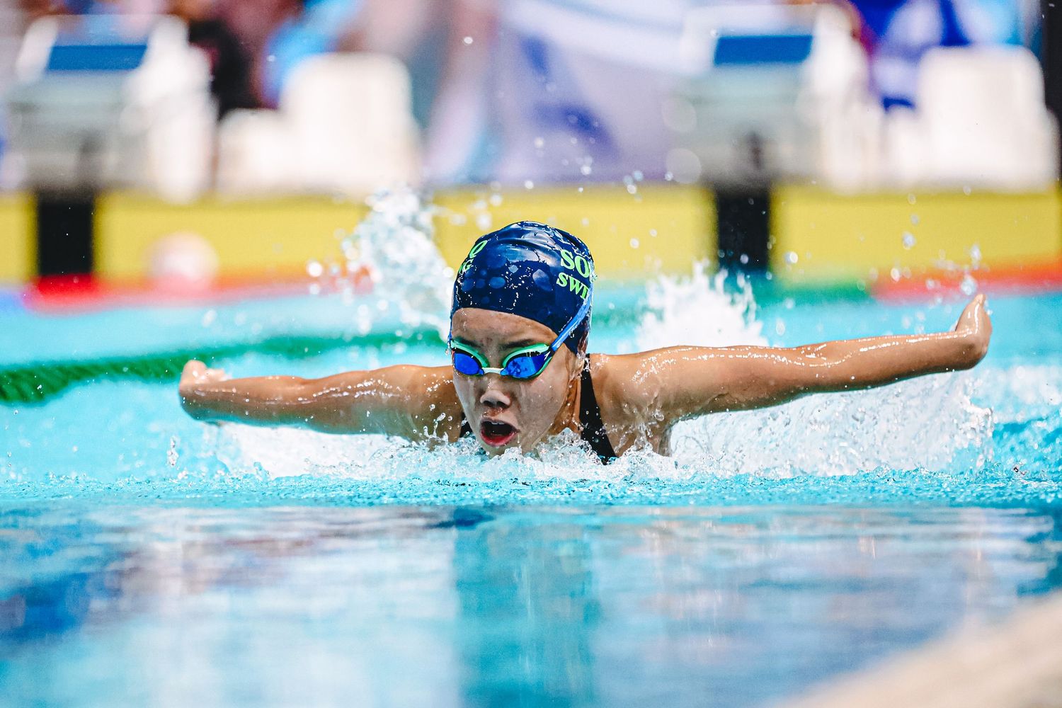 Swimmer performs backstroke in blue swimming pool with lane dividers during competition.