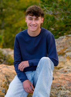 Person wearing navy blue sweater and light jeans sits casually on rocky outdoor terrain in natural setting.