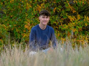 A person sits in tall autumn grass with colorful fall foliage visible in the background.