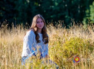 A person sits in a golden meadow wearing a white sweater with sunlit forest in the background.