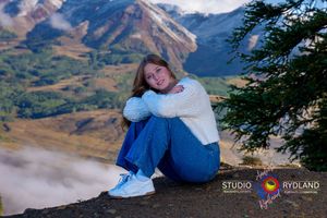 A cozy mountain scene with someone sitting on a hillside overlooking snow-capped peaks in the distance.