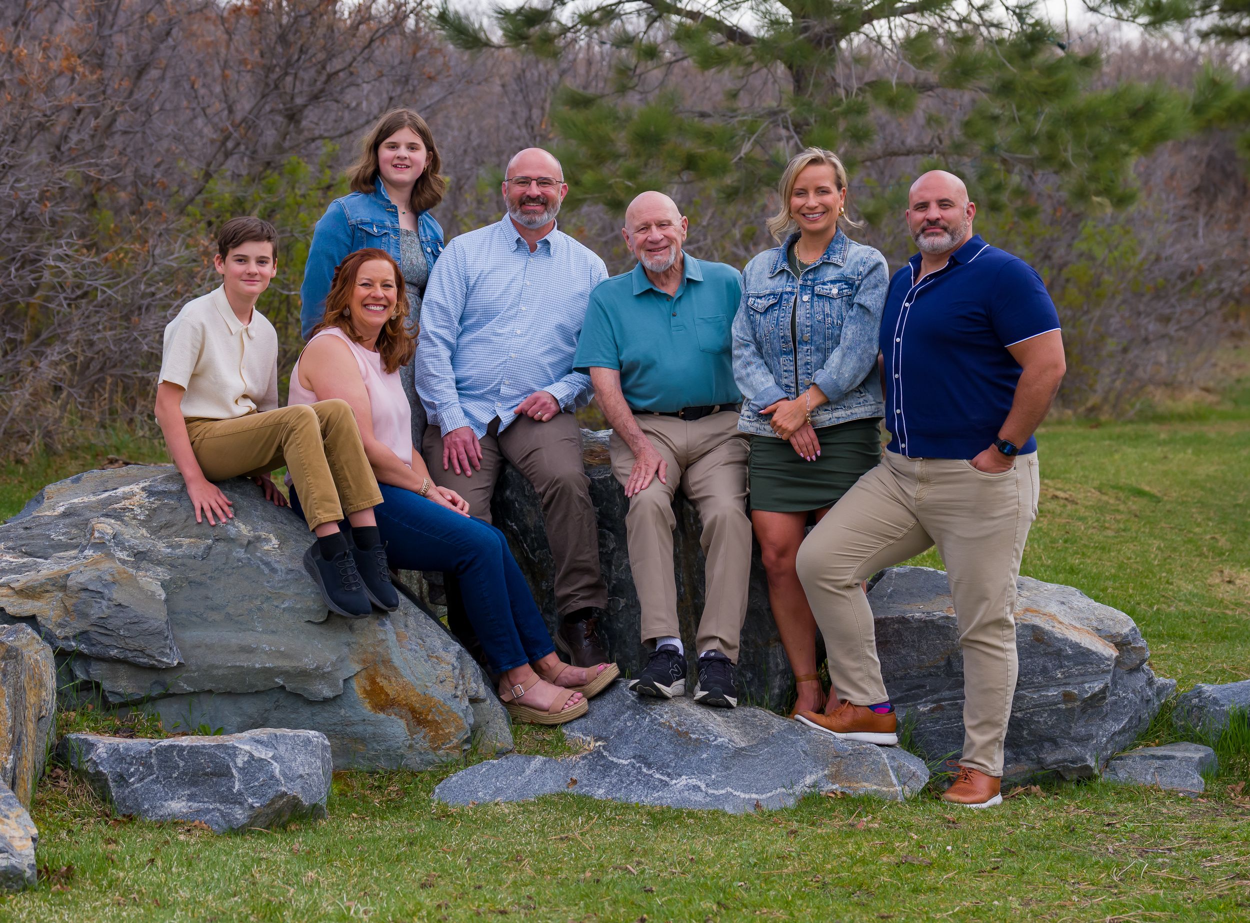 A series of casual outdoor family portraits taken on gray rocks with greenery and trees in the background.