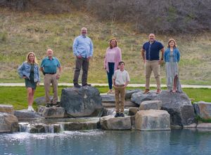 A group of people standing on large boulders beside a water feature in a natural outdoor setting.