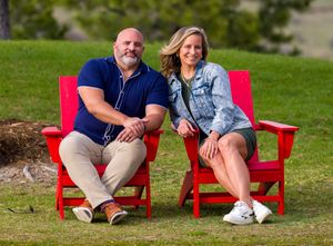 People sit on bright red benches outdoors on a grassy lawn in matching navy outfits.