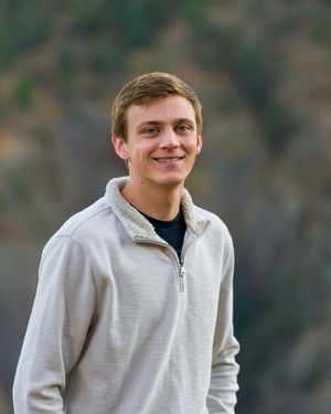 Young person wearing a light gray quarter-zip pullover sweater and black shirt outdoors with a blurred natural background.