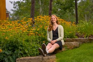 Person sits on garden bench surrounded by vibrant orange black-eyed susan flowers in lush summer garden setting.
