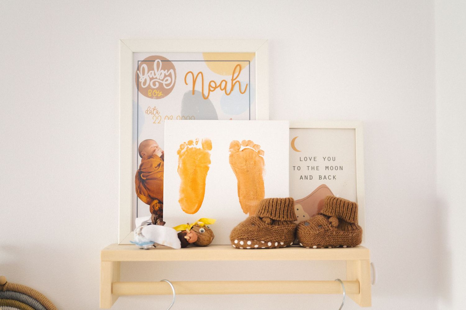 Baby's nursery shelf displays footprint art, brown leather boots, and a framed quote against a white wall.