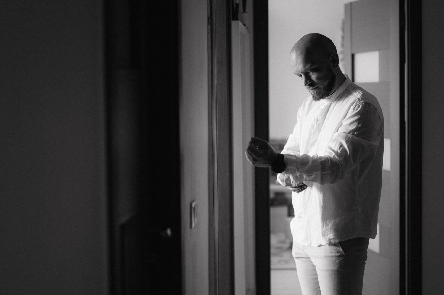 Black and white photo of person in casual white clothing standing by doorway while looking at phone.
