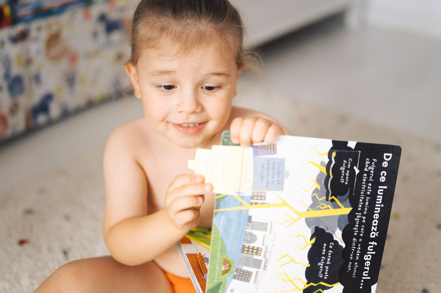 Young child sitting on floor reading through a colorful picture book with interest and joy.