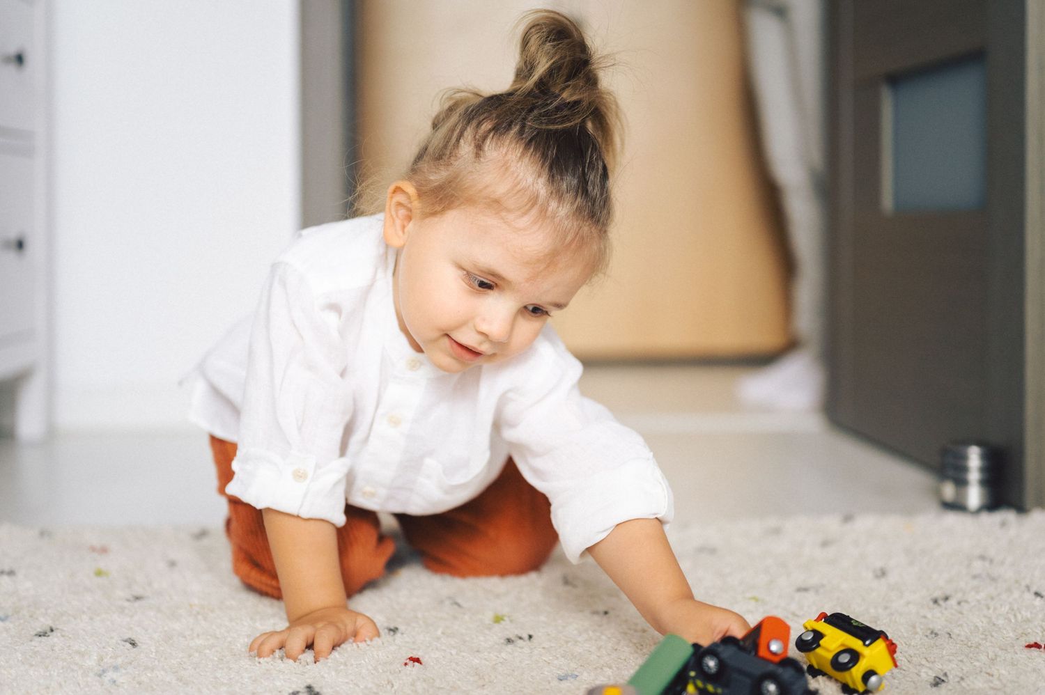 A child crawls on a light-colored floor while playing with colorful blocks and toys during indoor playtime.
