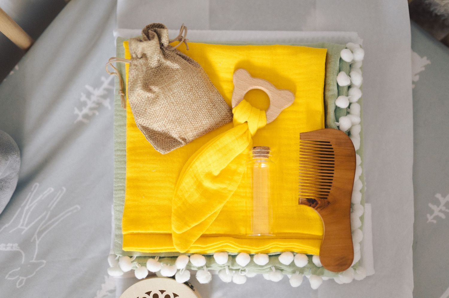 Baby care essentials laid out on yellow cloth including wash sponge, comb, and rubber toy.