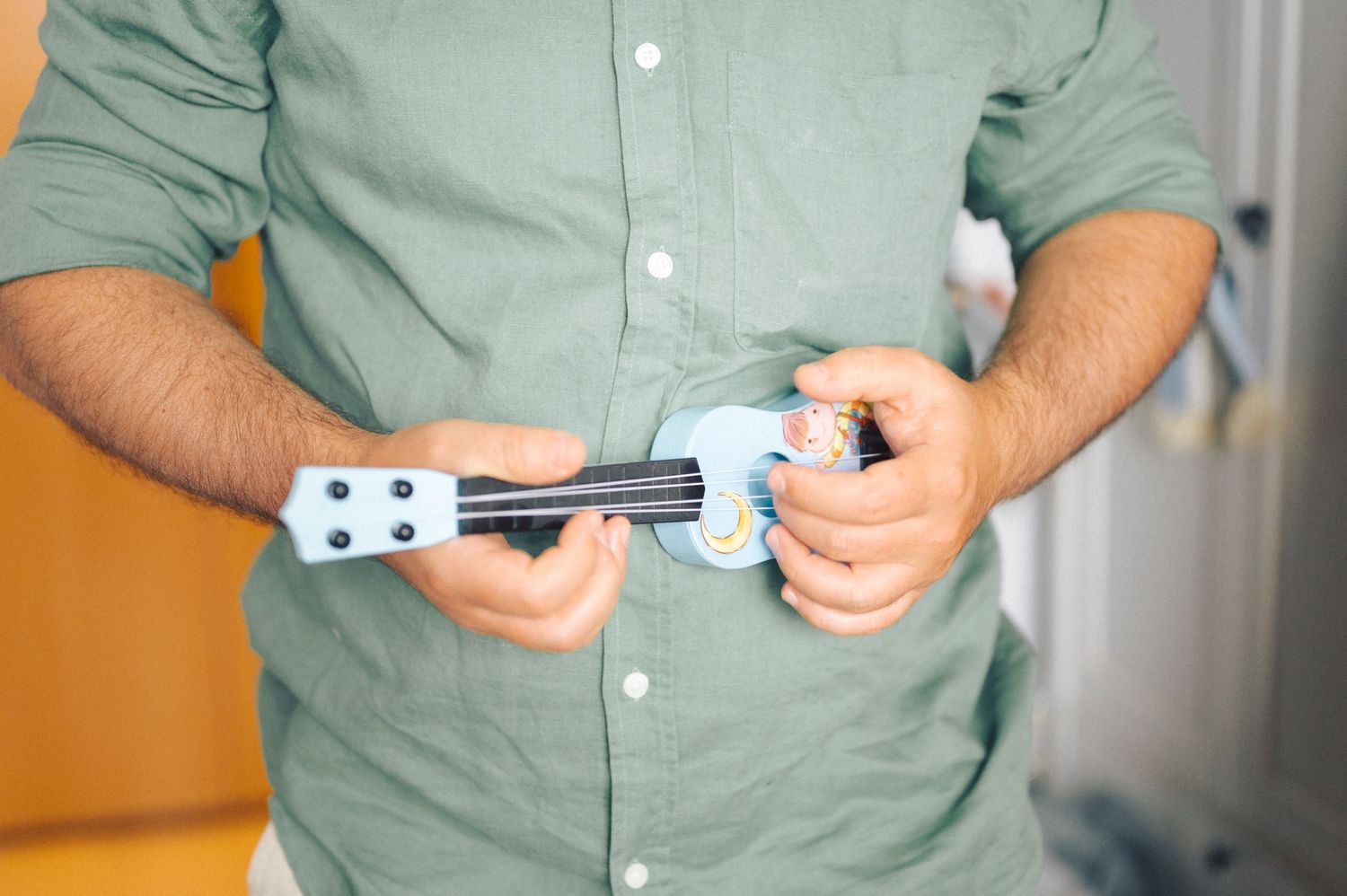 Person in sage green shirt examines a white video game controller against a bright background.