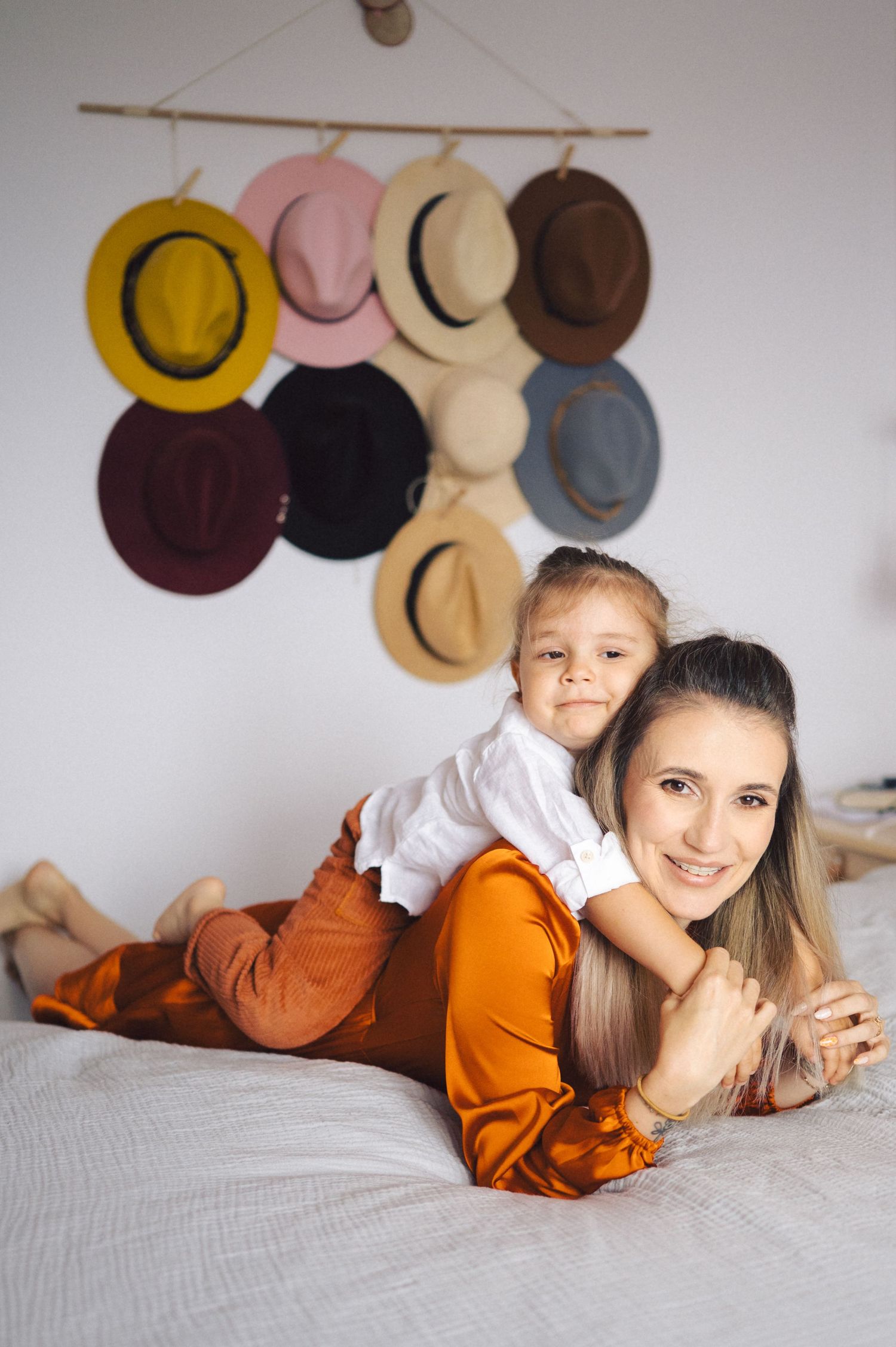 Person lying on bed wearing orange outfit with collection of colorful hats displayed on wall for home decor.