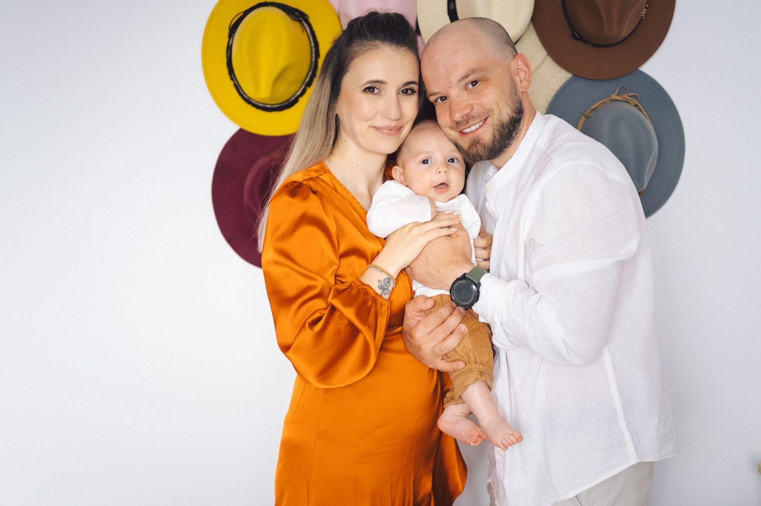 A family poses against a white wall decorated with hanging hats while wearing orange and white outfits.