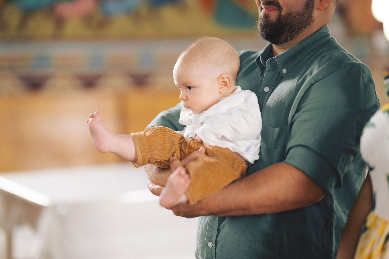 A baby wearing white sits on a caregiver's lap in a green shirt, creating a tender family moment.