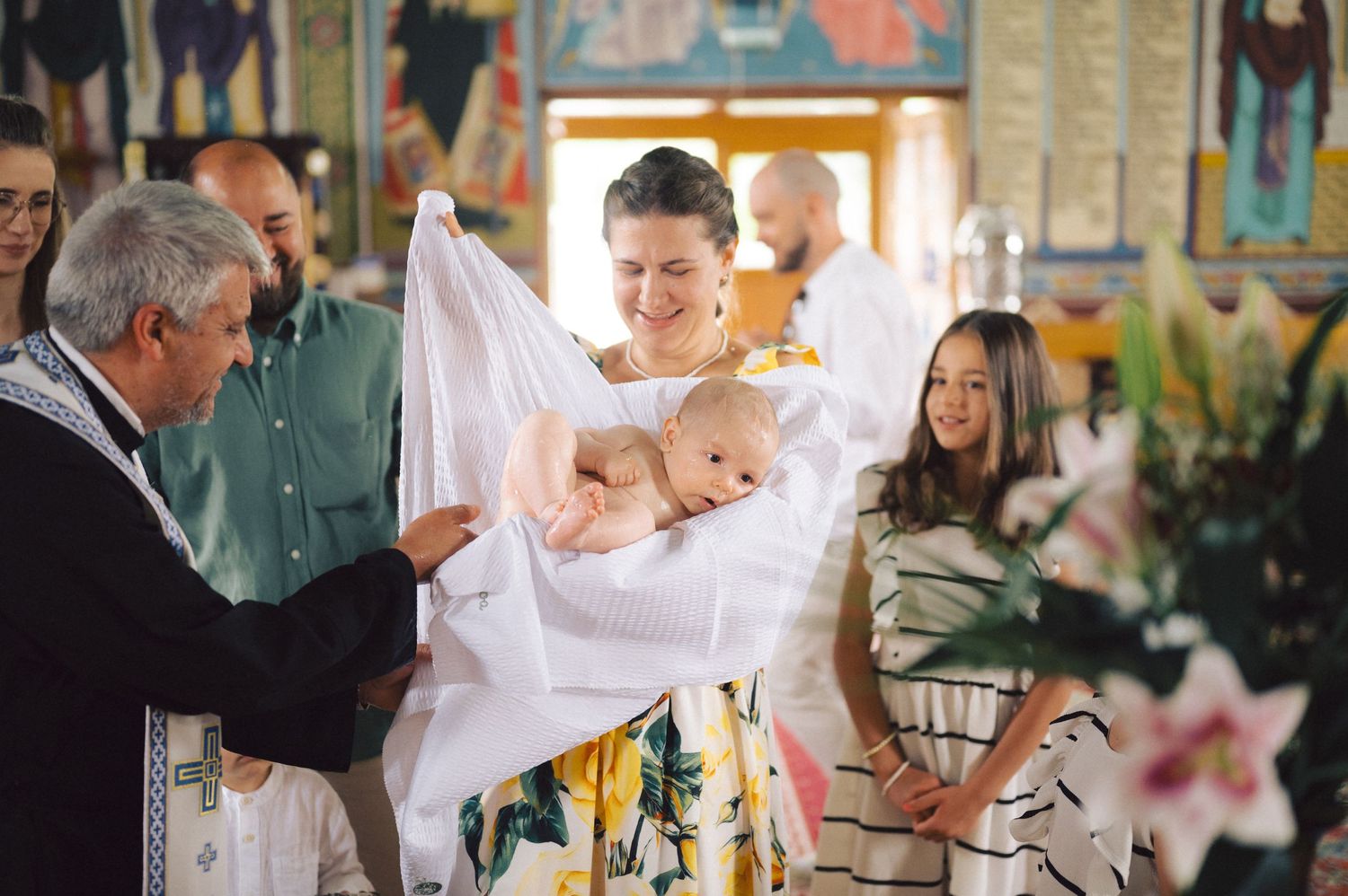 A baby's christening ceremony in a church surrounded by white lilies and decorative elements.