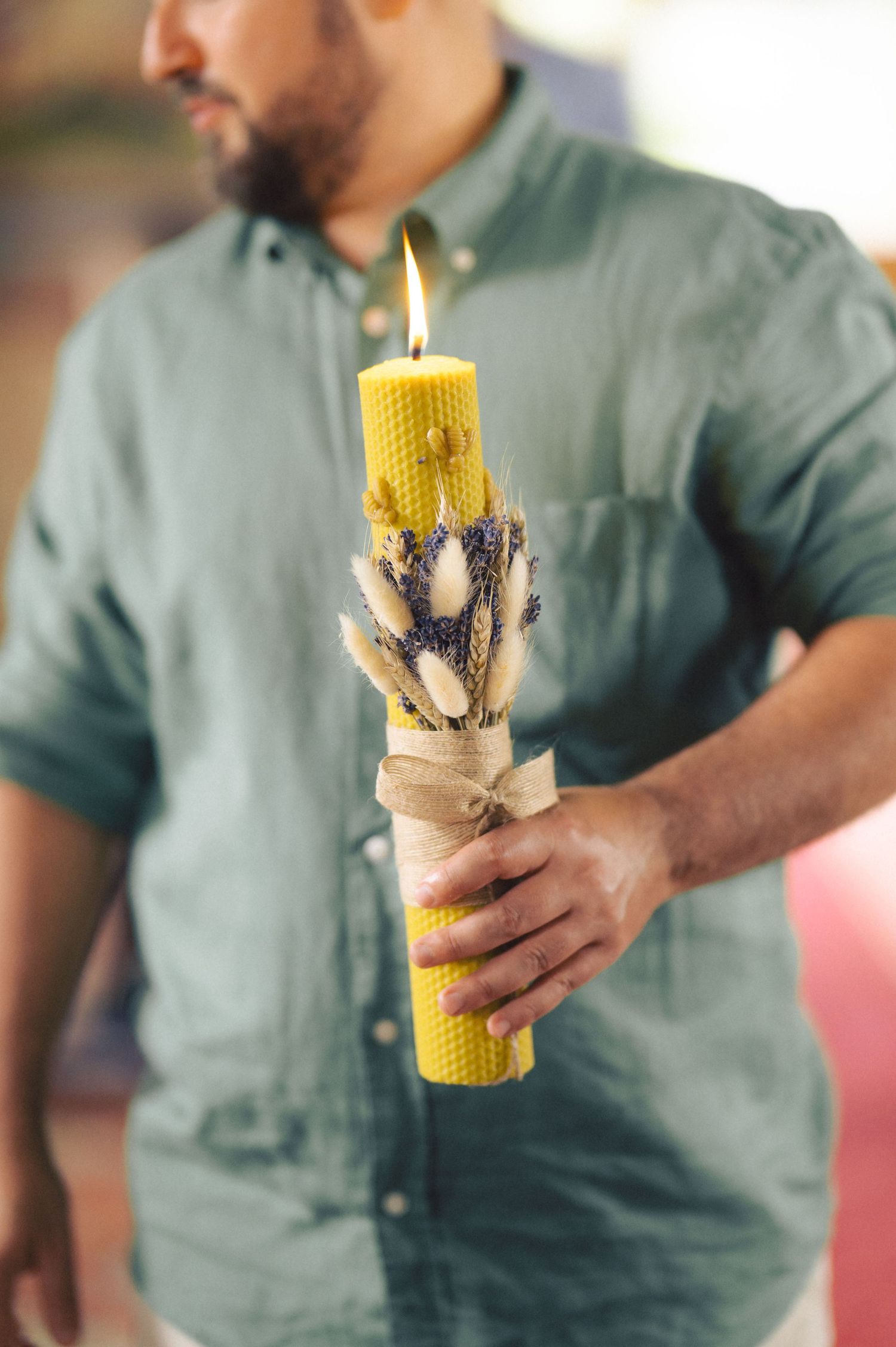 A hand holding a yellow beeswax candle with dried flowers decorating its handcrafted surface.