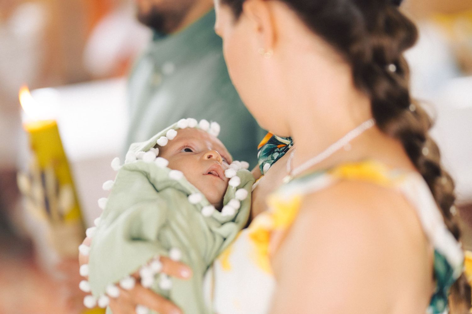 A newborn baby wrapped in a mint green blanket yawns while being held during feeding time.