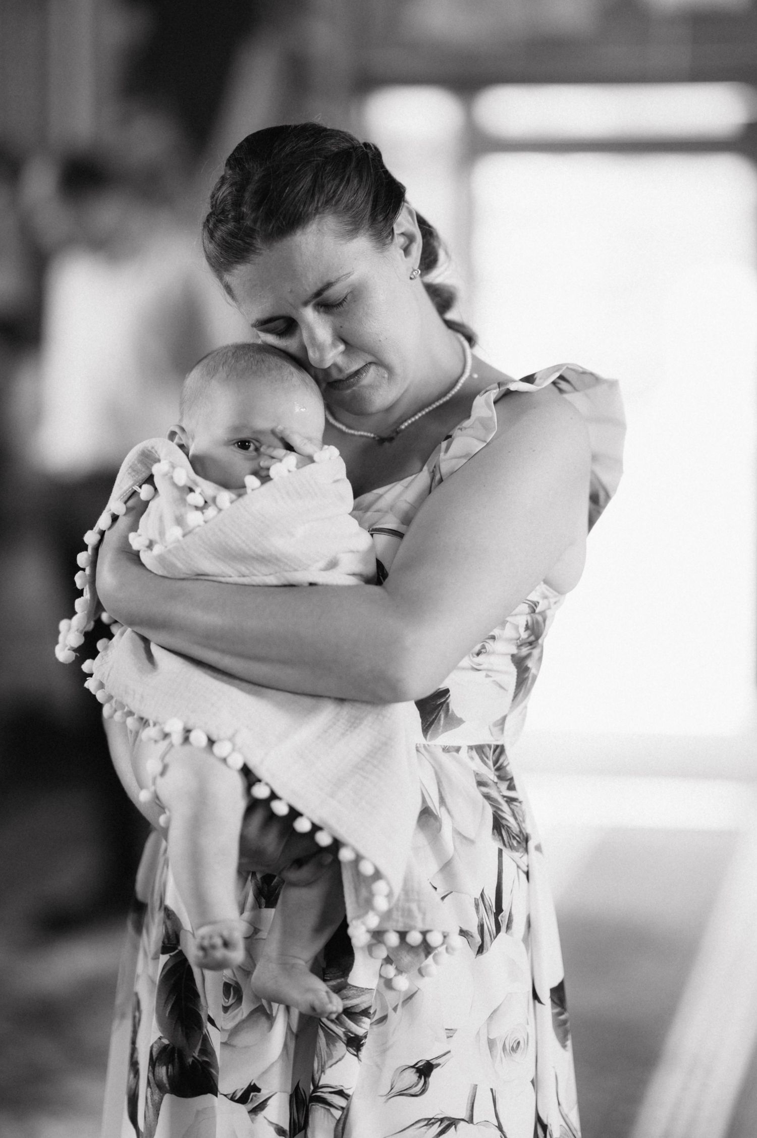 A tender black and white portrait of parent holding a sleeping baby wrapped in pom-pom trimmed fabric.