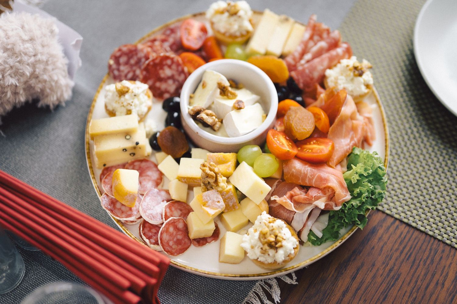 Assorted cheese, charcuterie, and appetizers arranged on multiple plates on a dark wood table.
