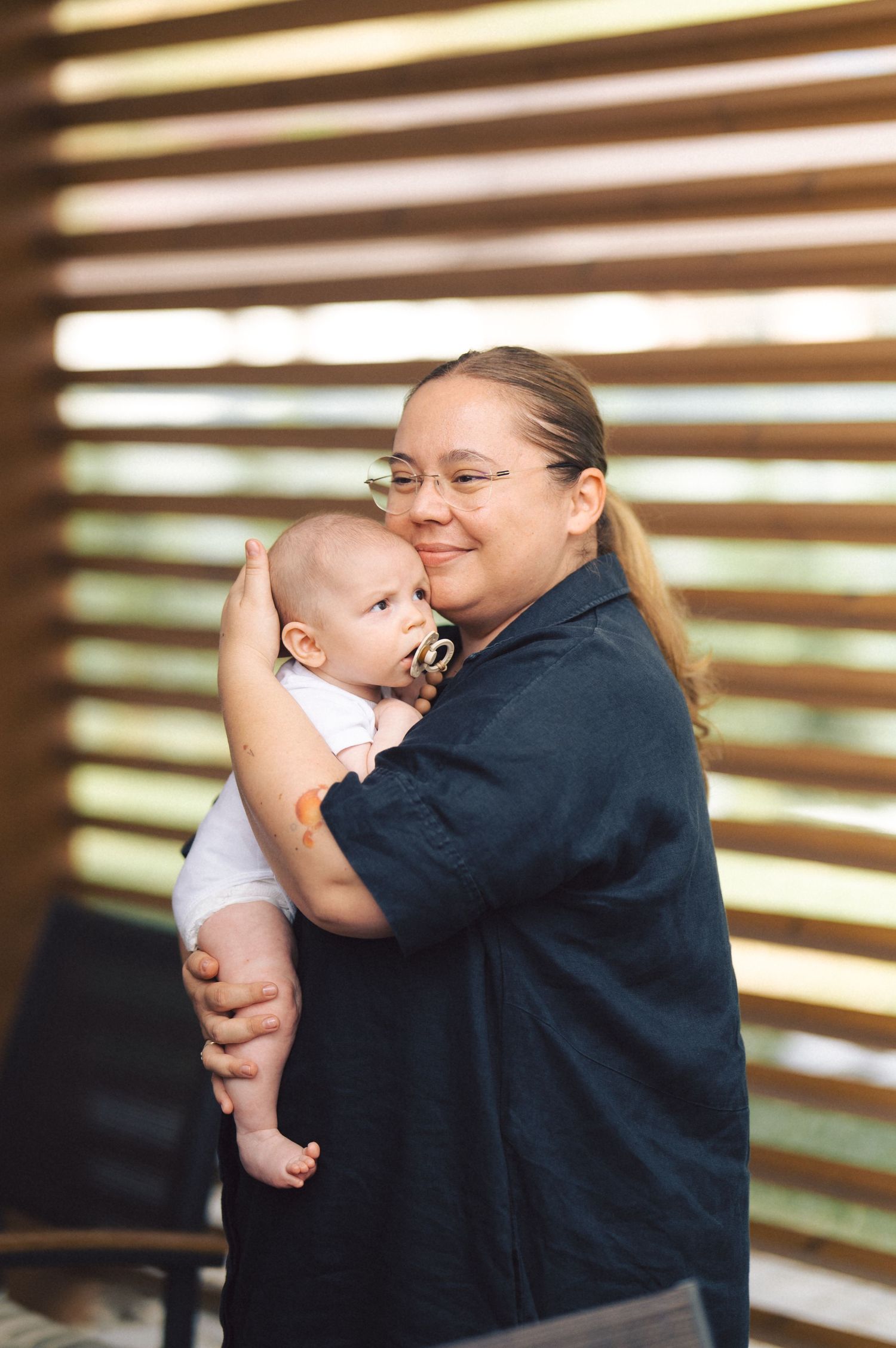 A tender moment as an adult holds a baby in front of a slatted wooden backdrop in natural lighting.