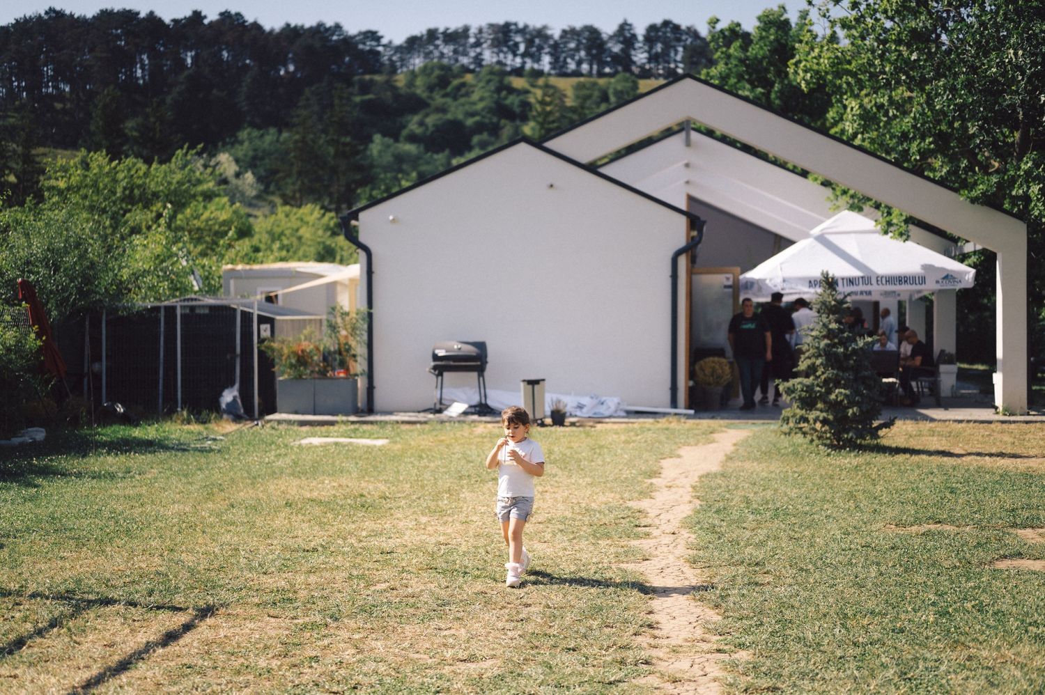 A panoramic sequence of images showing a large backyard with white buildings and grassy areas on a sunny day.