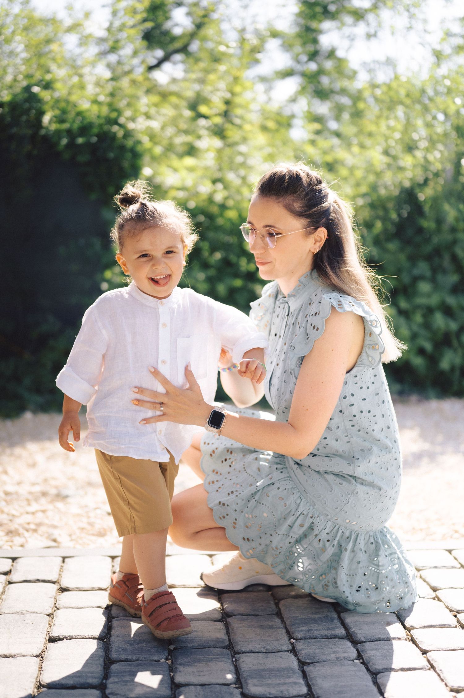 A parent and child share a tender moment together outdoors on brick paving in warm sunlight.