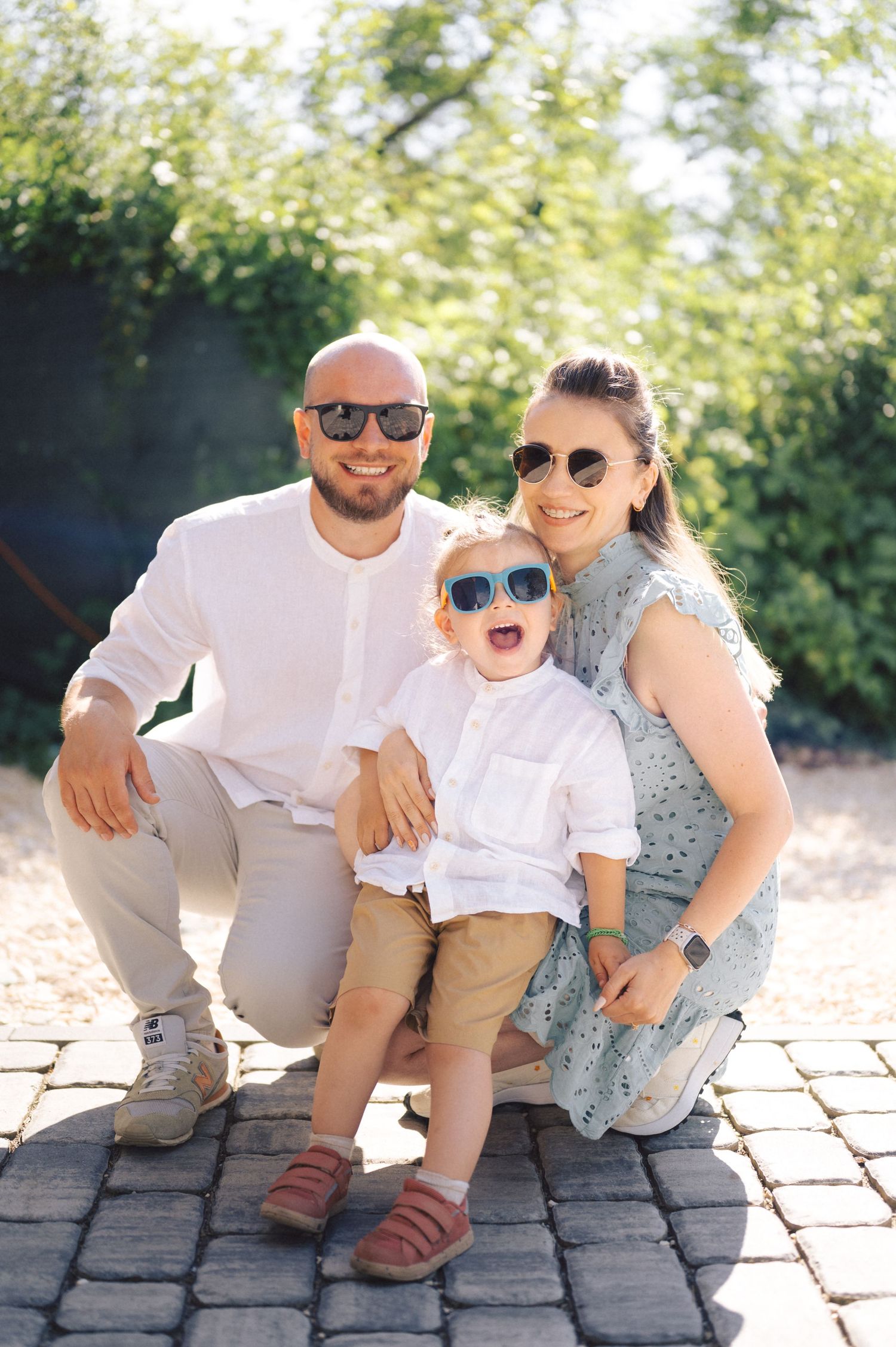 Happy family wearing sunglasses pose together on cobblestone patio on sunny summer day.