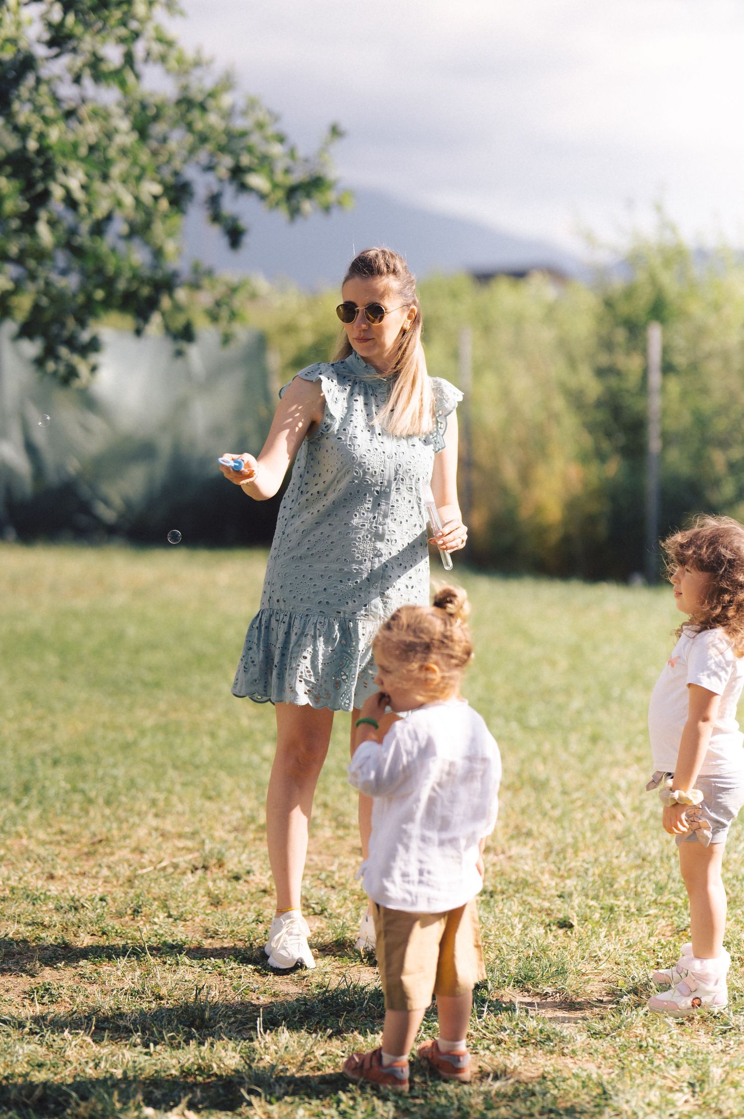 Sun-dappled outdoor scene showing playful family moments in a grassy meadow on a bright summer day.