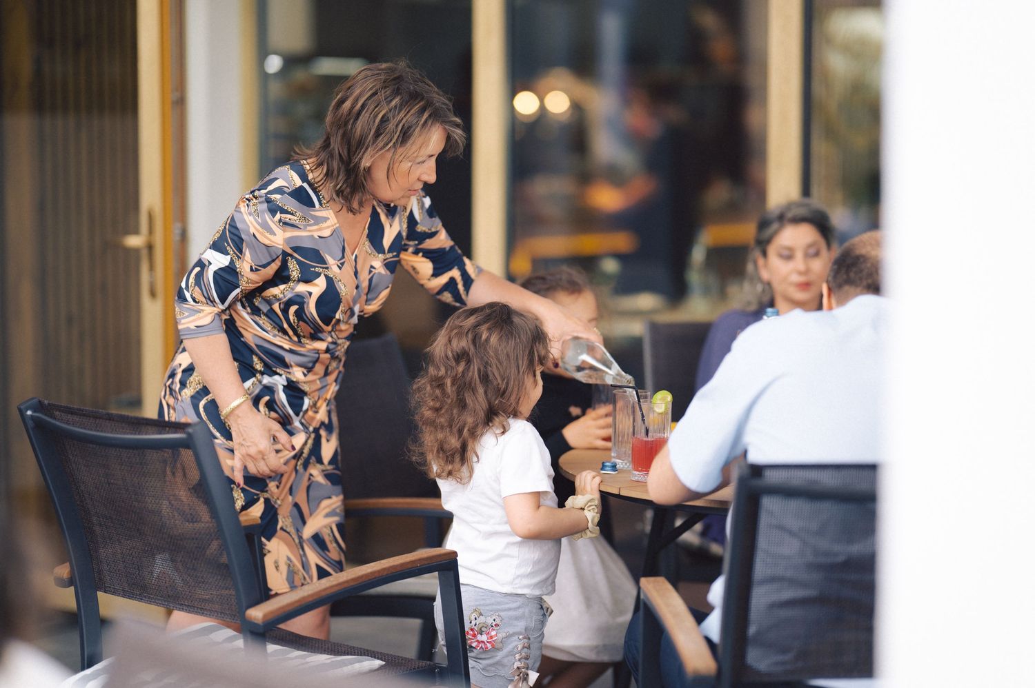 A caring interaction between adults and a child at an outdoor cafe restaurant setting.