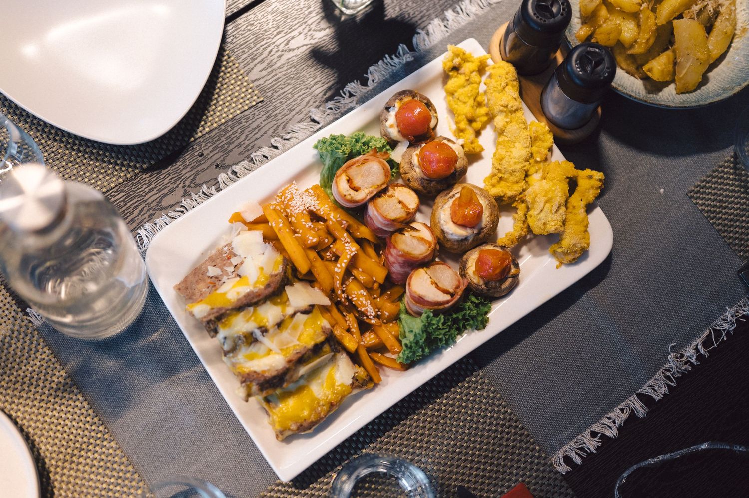 Assorted plates of colorful appetizers and snacks served on white rectangular platters arranged on a dark table.