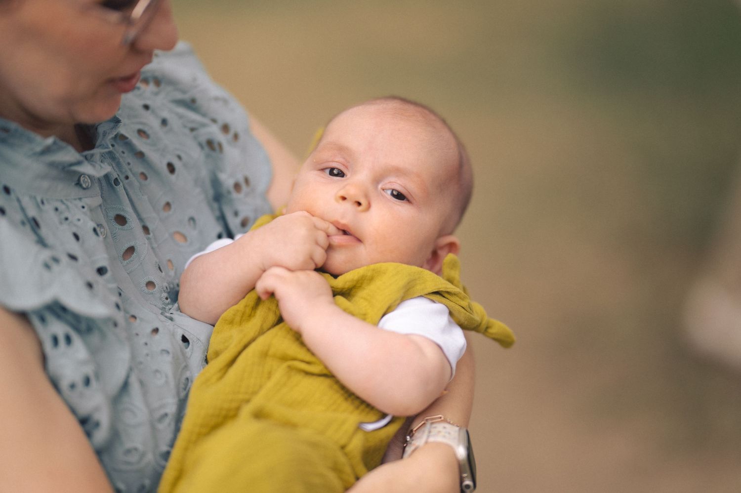 A person holding and playing with a small infant wearing a yellow outfit.