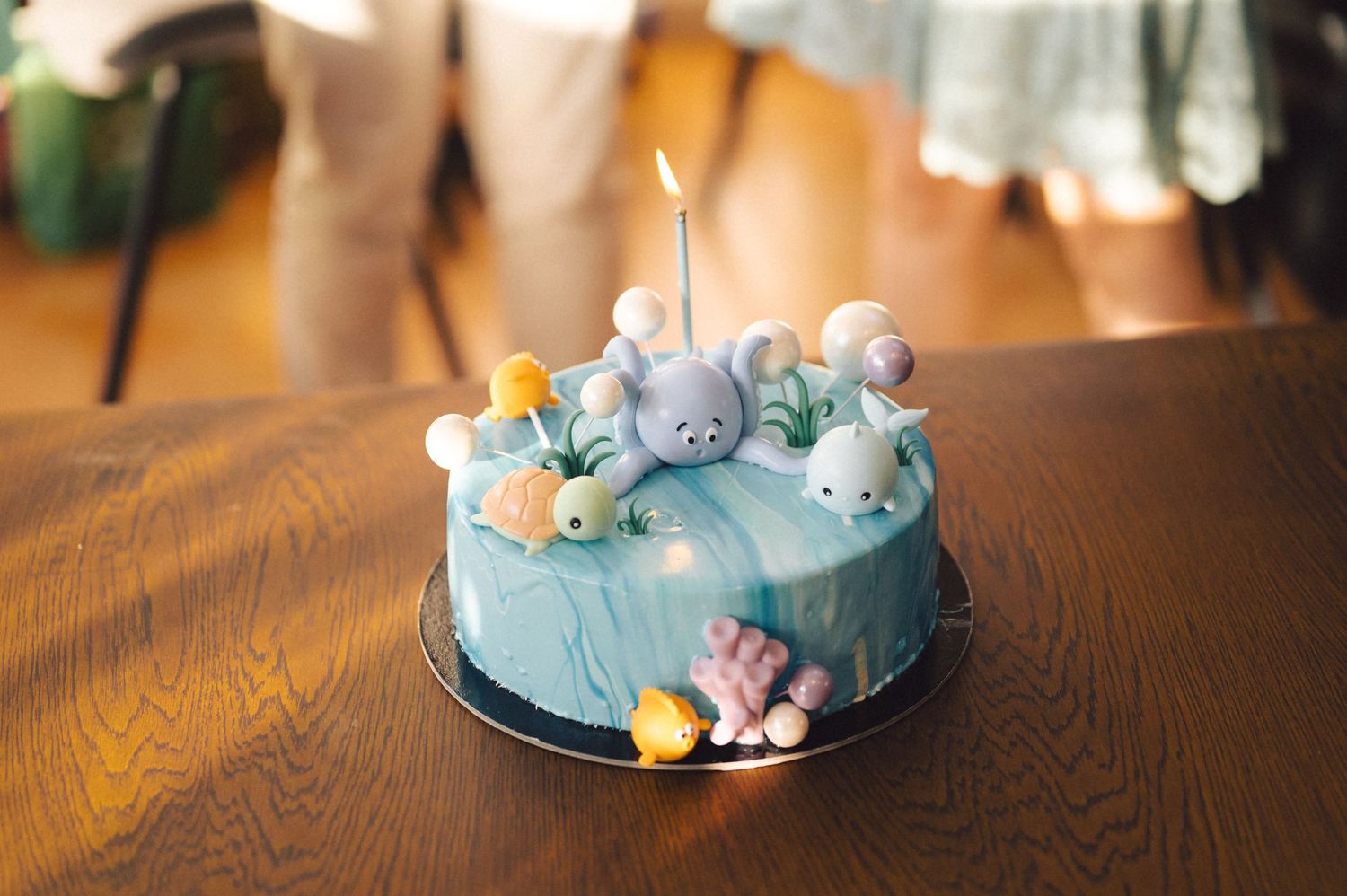 A blue and white elephant-themed birthday cake with candles displayed from multiple angles on a wooden surface.
