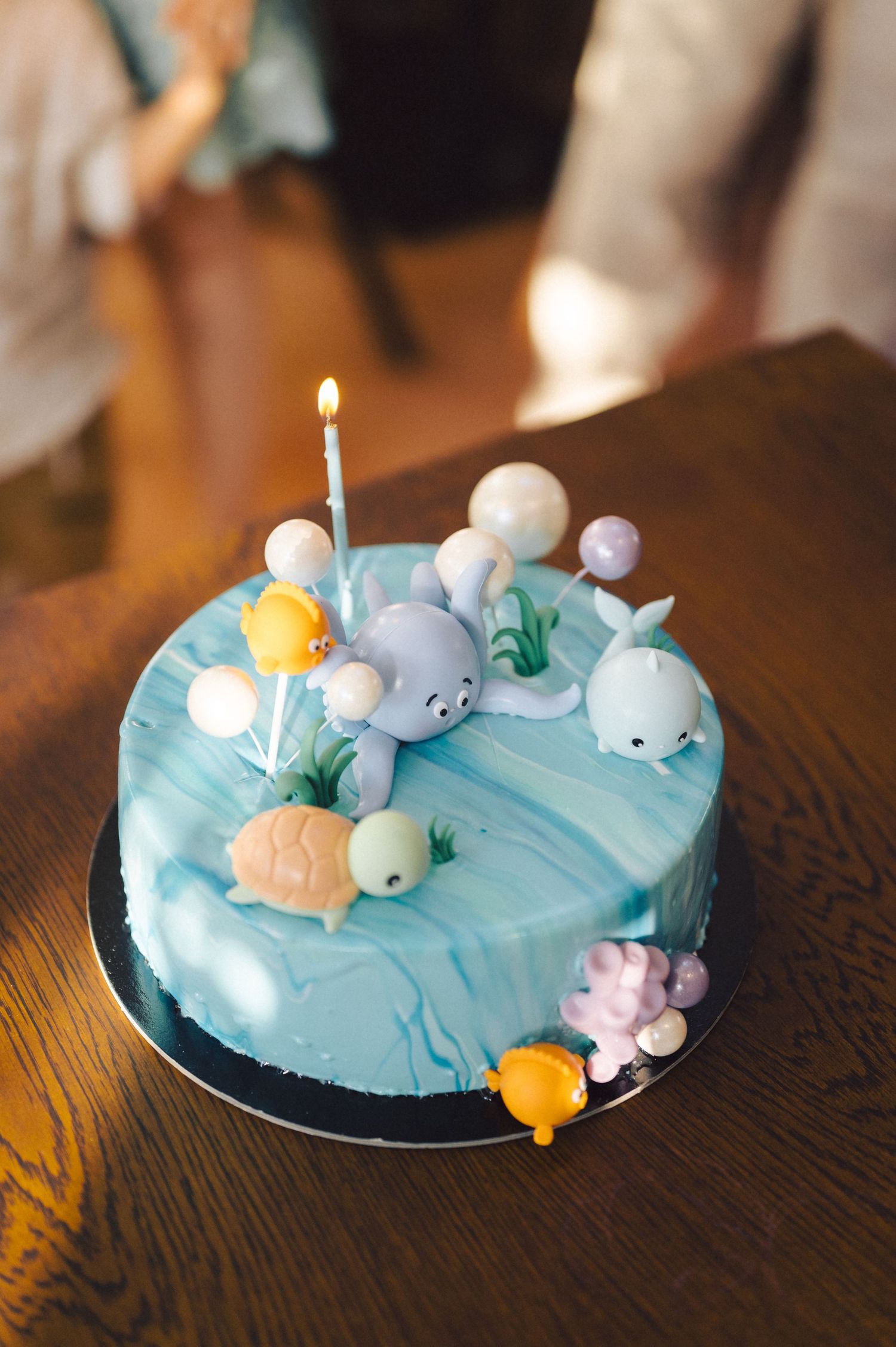 Blue frosted cake decorated with adorable sea-themed fondant creatures including whales, seals and fish on a wooden table.