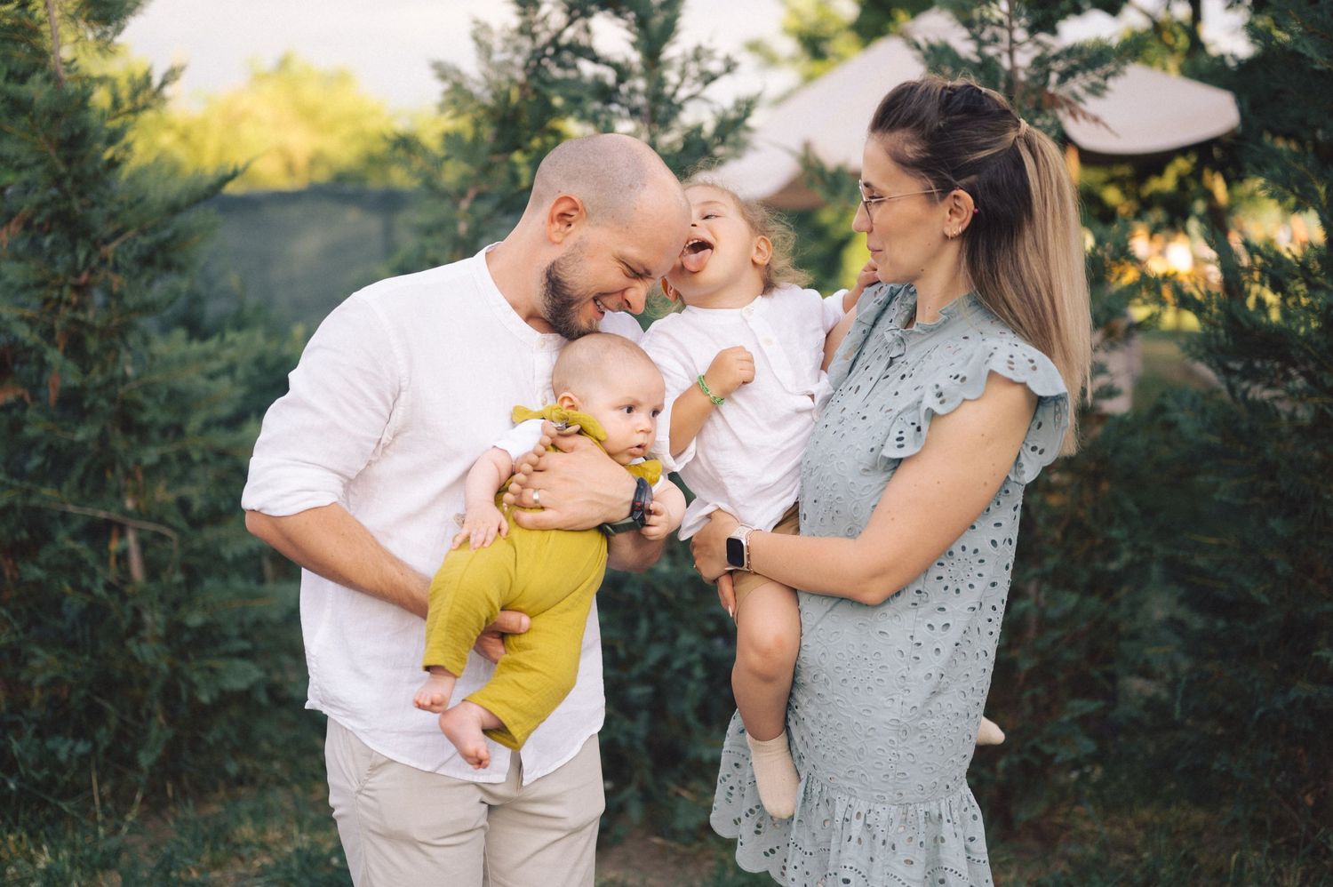 A tender moment between family members standing among evergreen trees at sunset during a golden hour photo session.