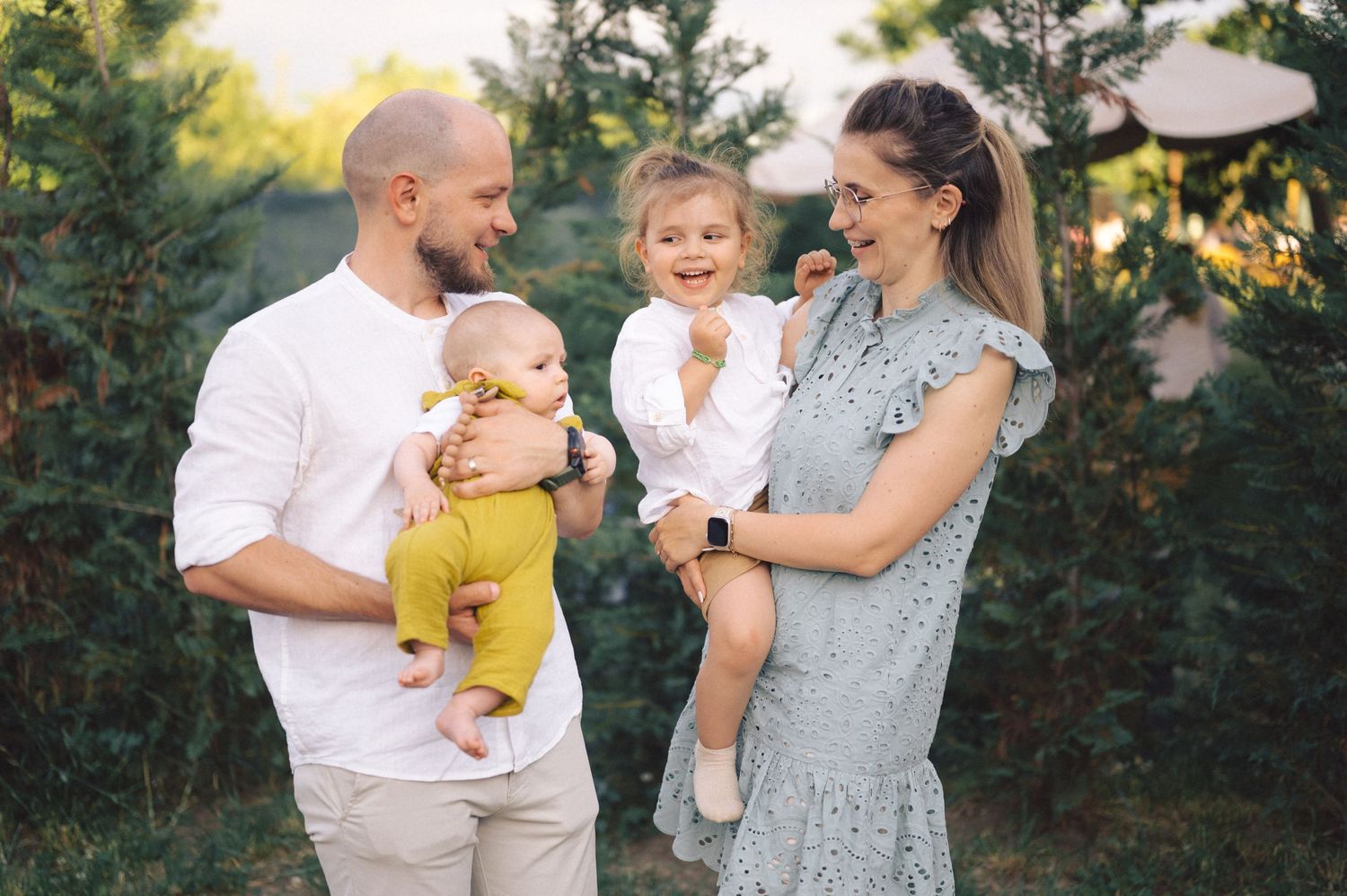 A loving family wearing coordinated white and yellow outfits shares joyful moments in a lush outdoor setting during sunset.