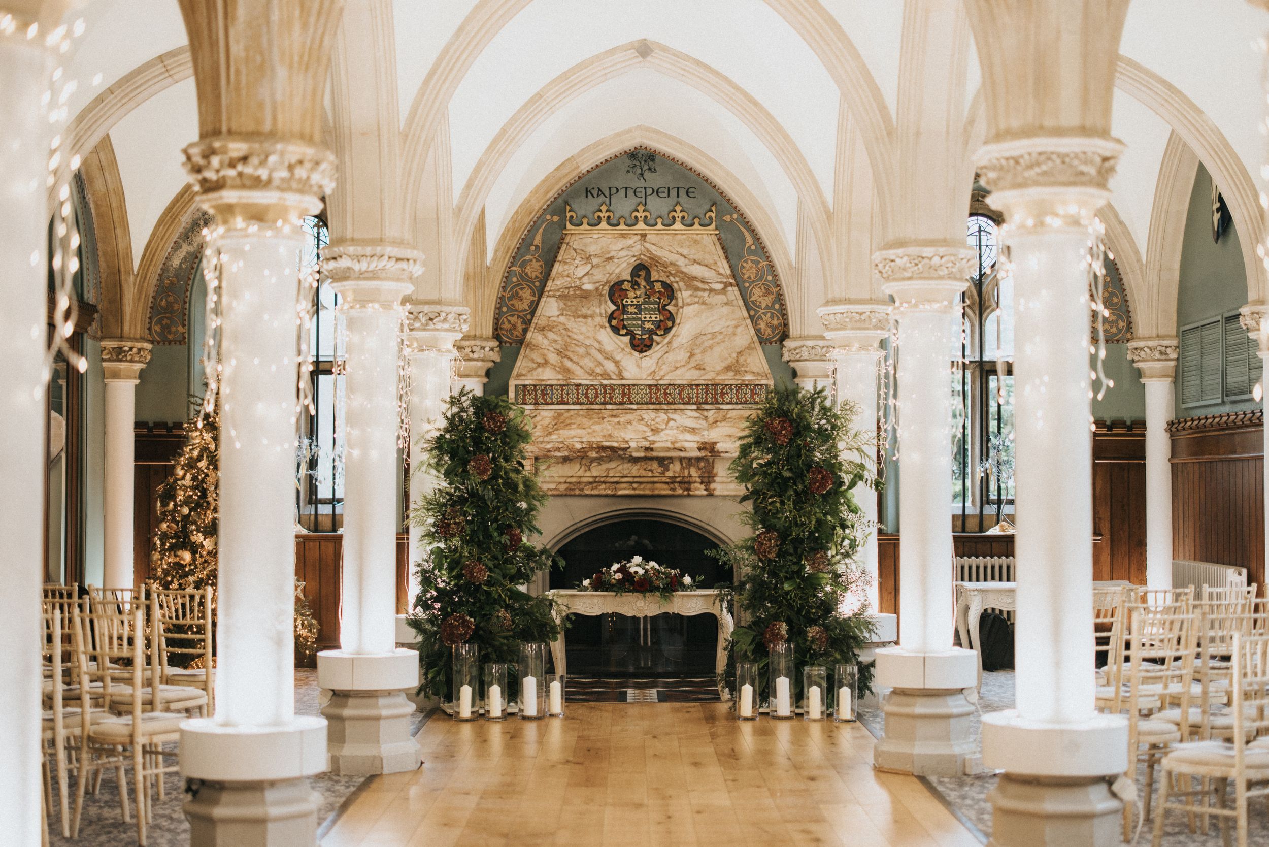 Elegant wedding venue interior with marble columns, arched ceilings and potted trees framing an ornate altar area.