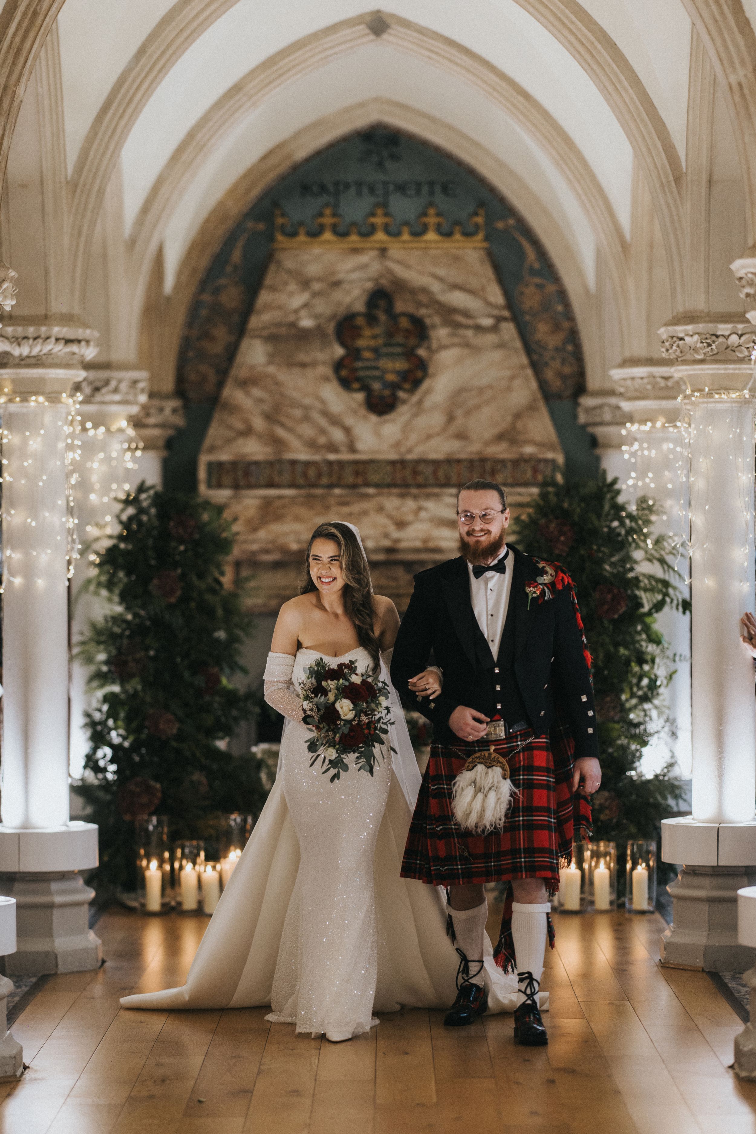 An elegant Scottish-themed wedding ceremony in a gothic arched church with glowing candles and evergreen decorations.
