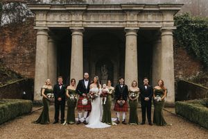 Wedding party poses in front of a classic stone colonnade with formal attire and traditional Scottish kilts.