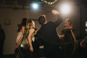 People dancing at a dimly lit party with light effects visible in the background, creating a festive atmosphere.