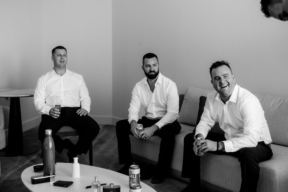 Three men in white button-down shirts sit casually together in a black and white photo.