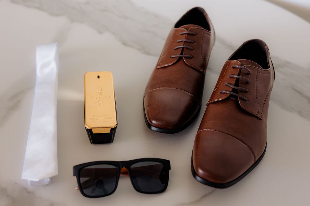 A pair of brown leather dress shoes arranged with black sunglasses and a gold cell phone on a light surface.
