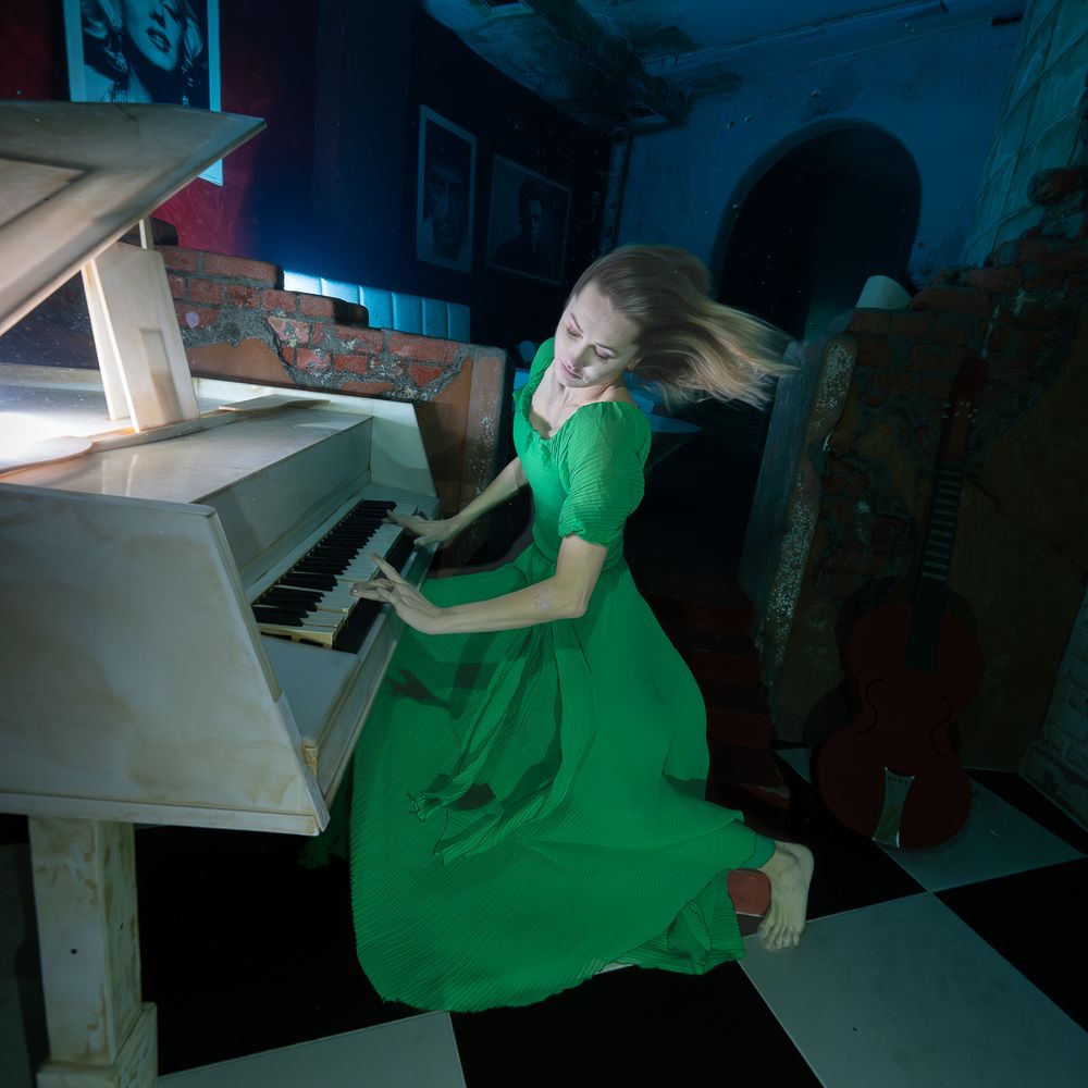 Three dark and moody photos show someone in a flowing green dress reclining on a white piano.