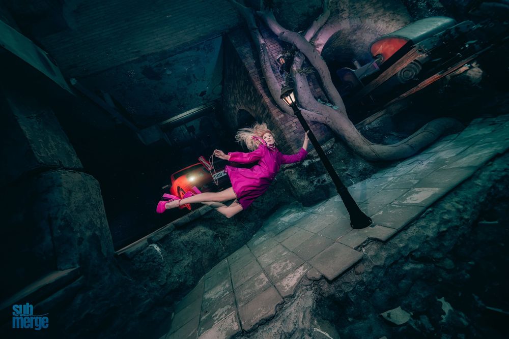 A person in pink clothing lies dramatically on a dark staircase in an artistic portrait composition.