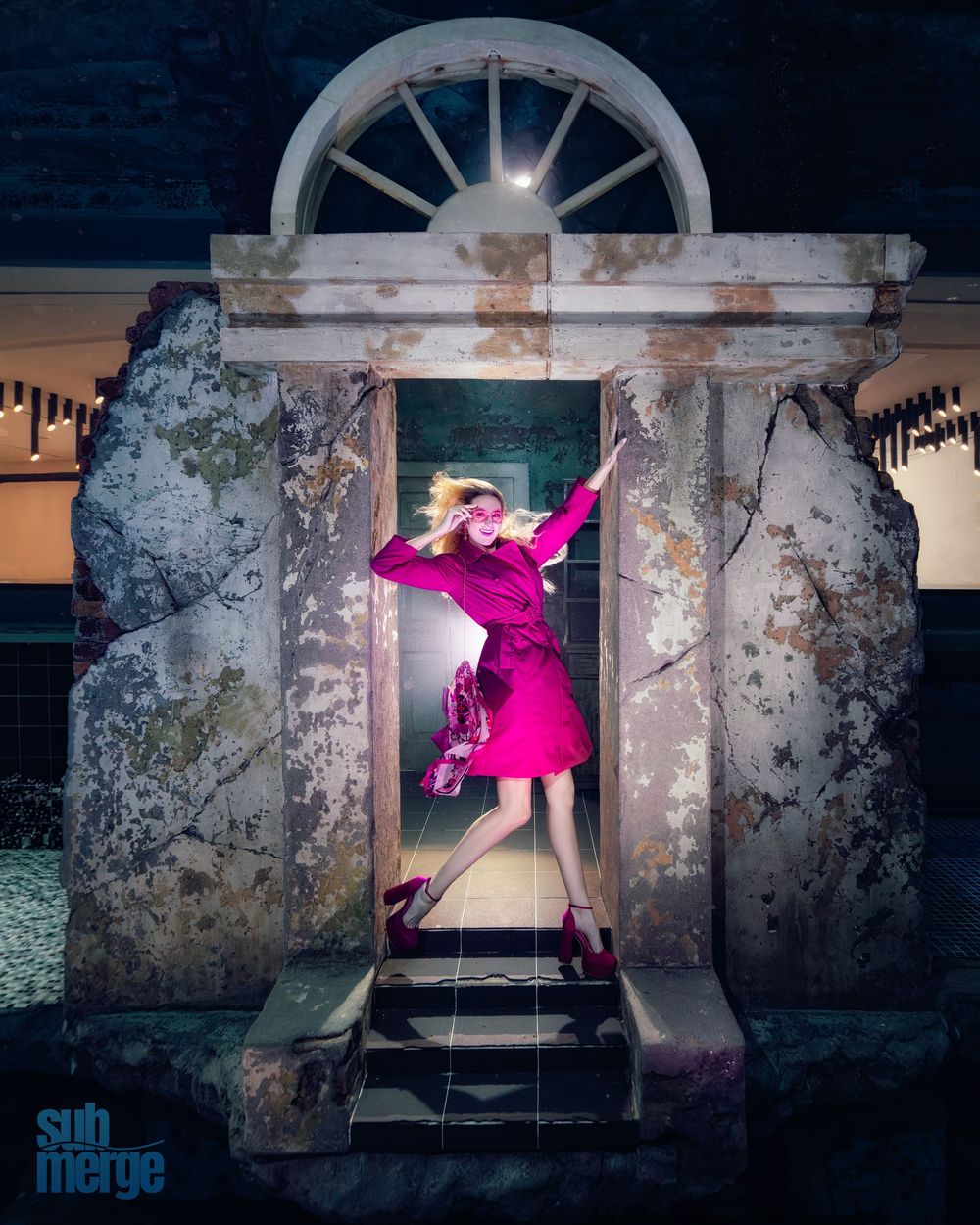 A figure in a vibrant pink dress poses dramatically in a stone archway at night.