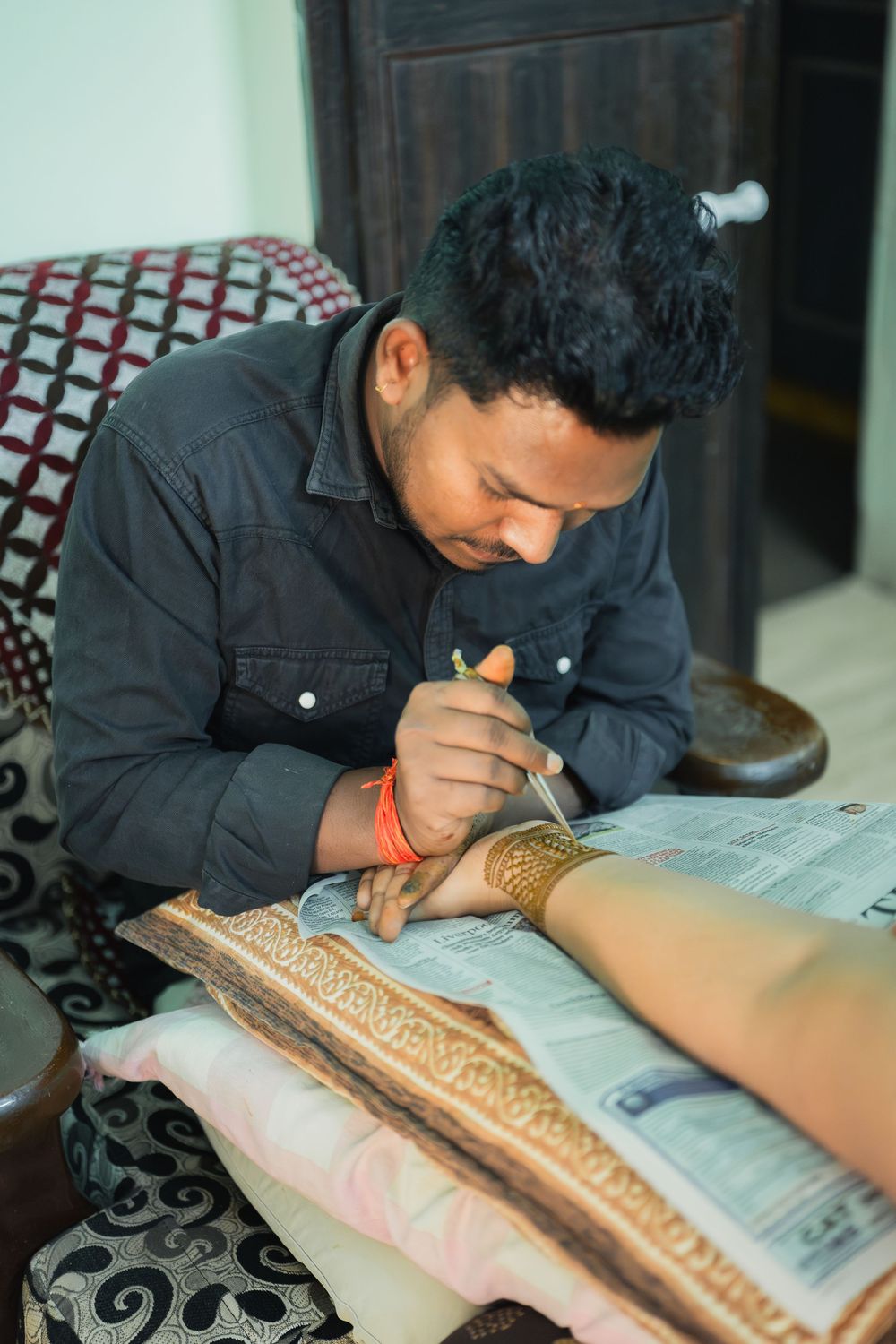 Artist carefully applying intricate henna design on someone's hand over newspaper.
