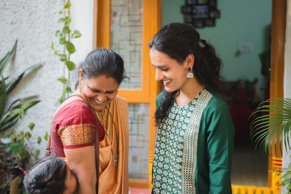 Two women in traditional Indian attire share a joyful moment outside a home.