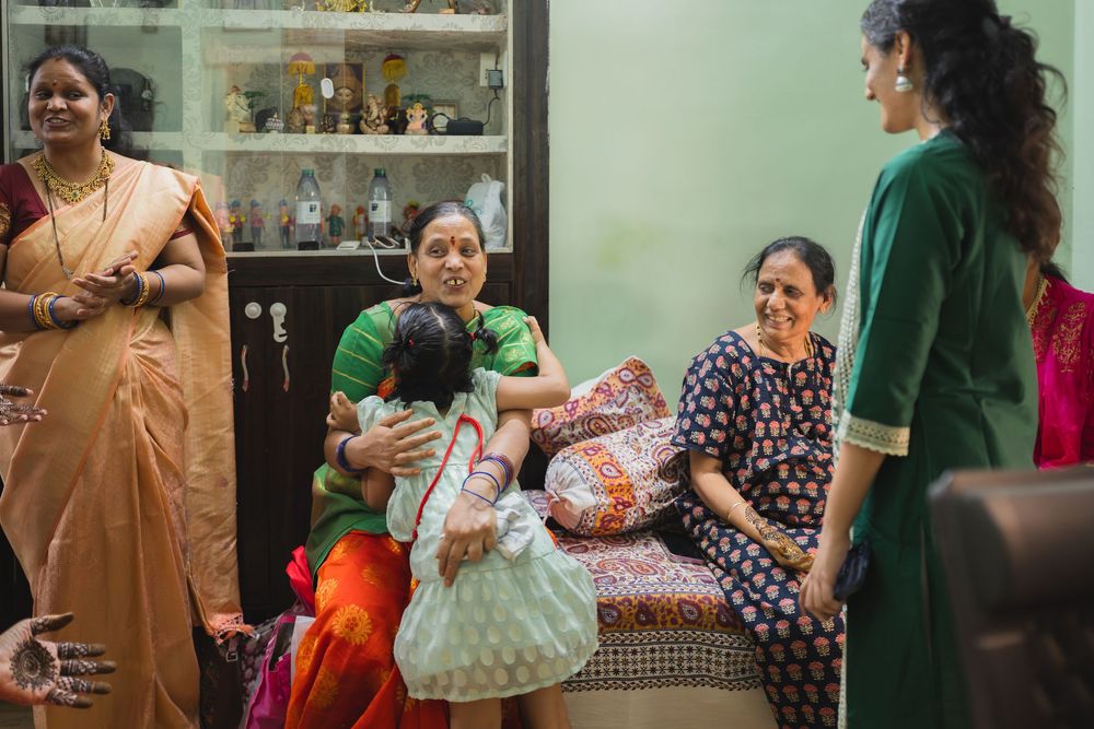 A group gathers in a living room with decorative shelving and traditional Indian furniture.