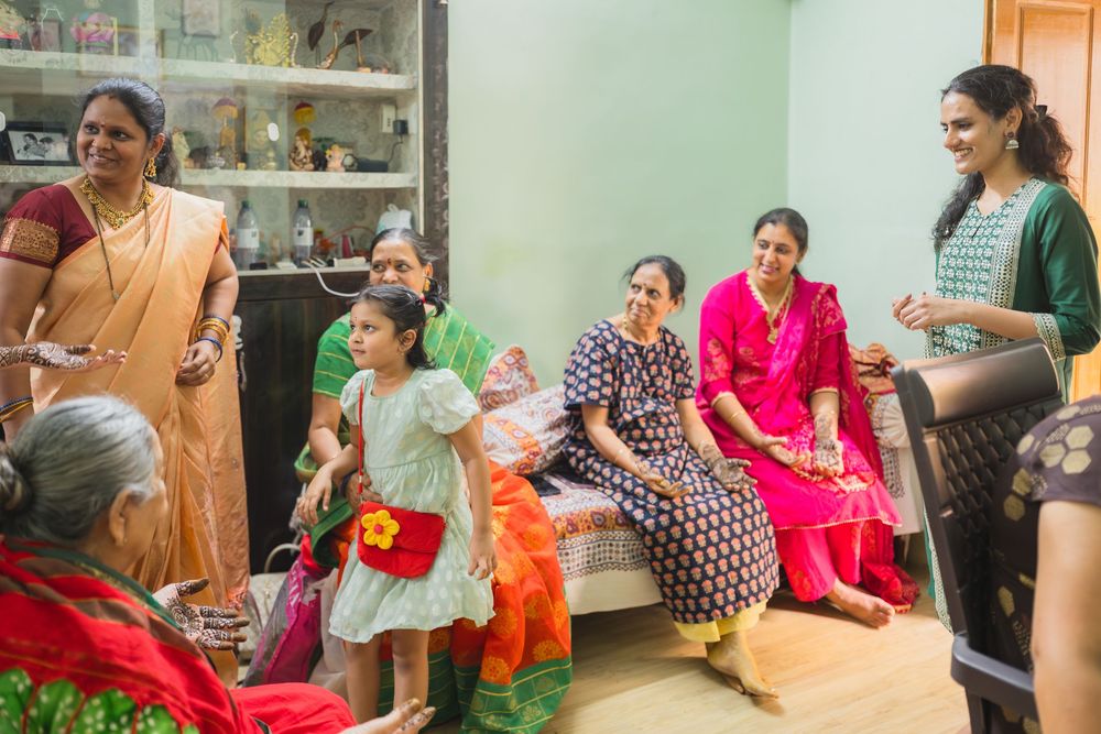 Family gathering in a living room with shelves of decorative items, wearing traditional Indian clothing.