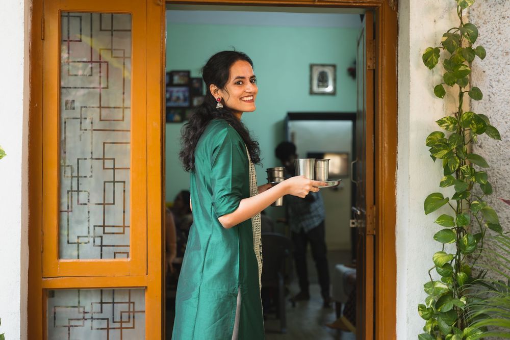 A person in an emerald green outfit holds a coffee cup while standing in a doorway with geometric window design.